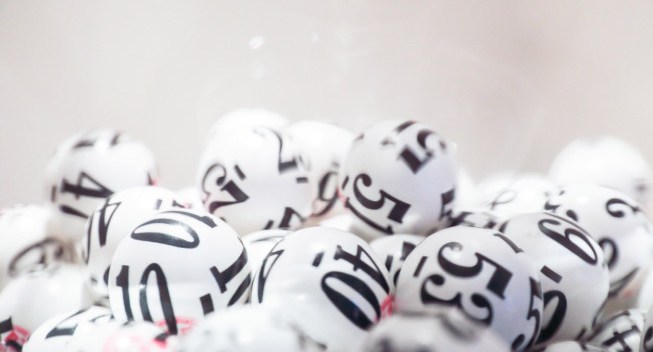 Many white lottery balls with black numbers on them are close together. Close up shot is taken against a white background. Taken by Canon 5D Mark lv.