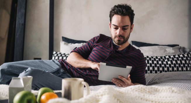 Morning routine: a man  using his digital tablet in bed in the morning.