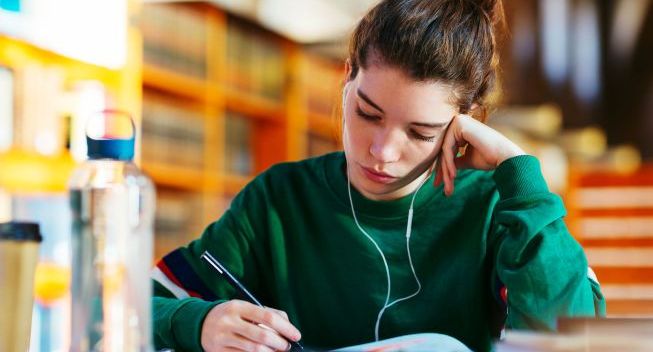 Young woman with earphone studying on library.
