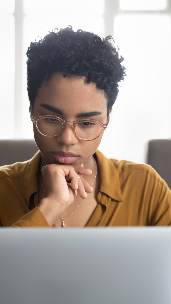 Young Black woman looking contemplative while using her laptop.