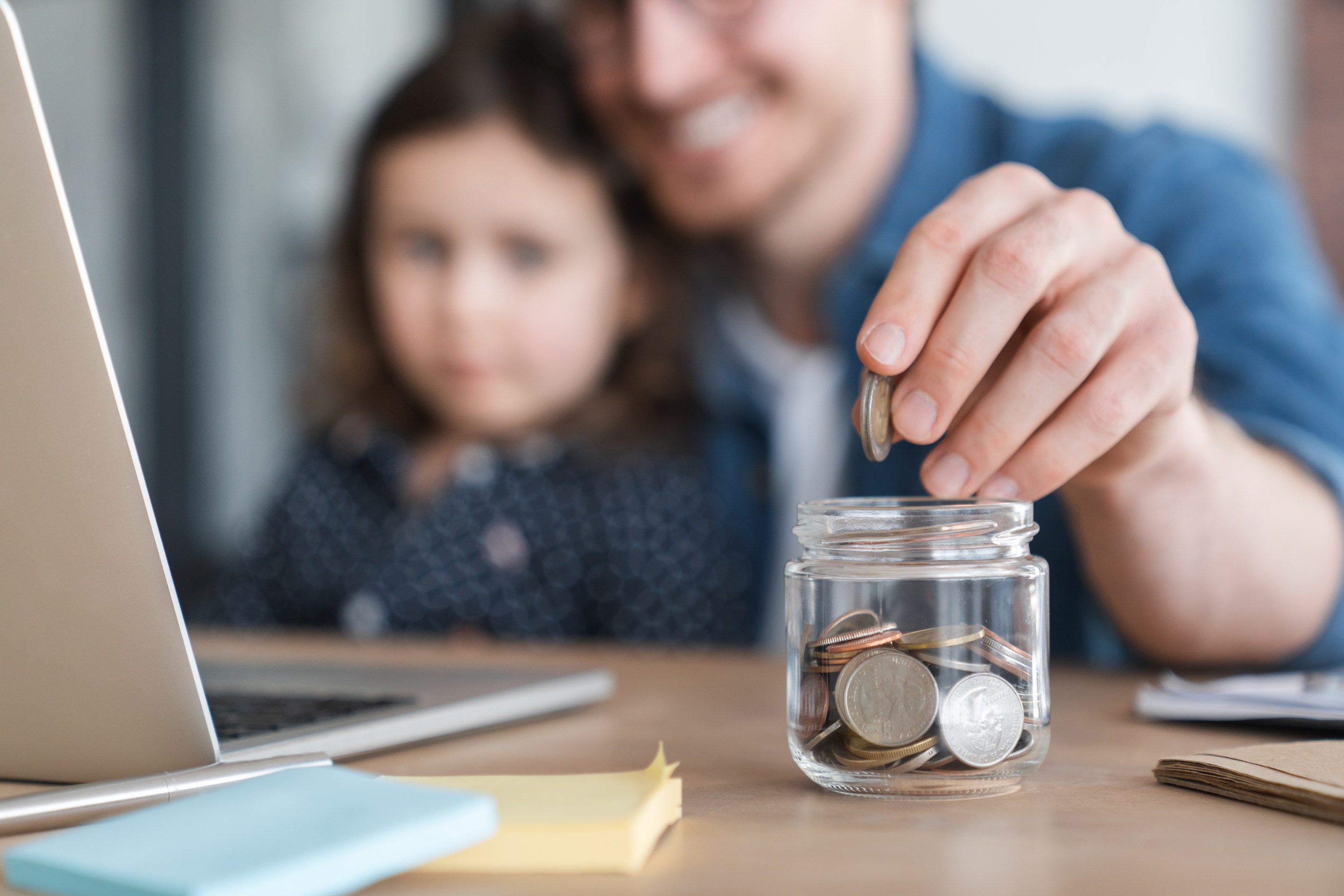 Dad with daughter in lap putting change in a jar.