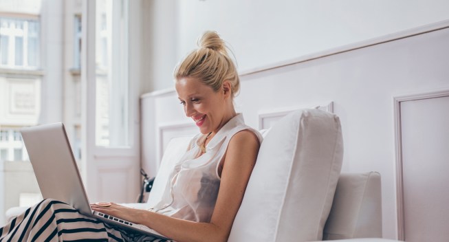 Smiling Caucasian woman sitting on her sofa and using her laptop.