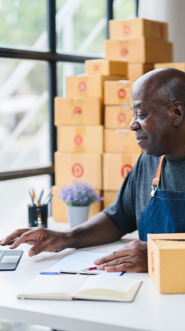 Black business owner working in front of laptop and packing boxes.