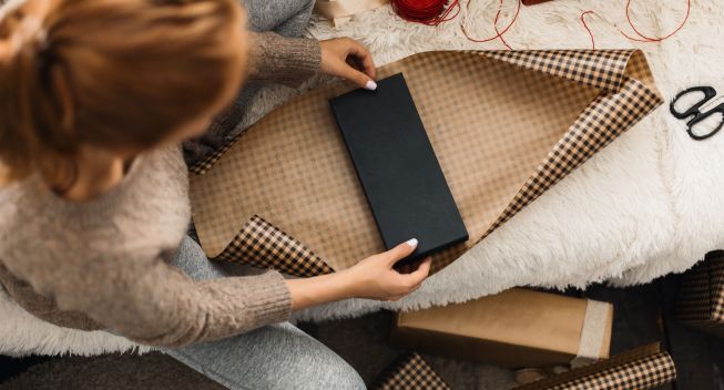 Young redhead woman wrapping Christmas Gifts at home