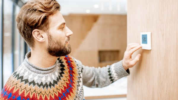 Man wearing a sweater adjusting thermostat.