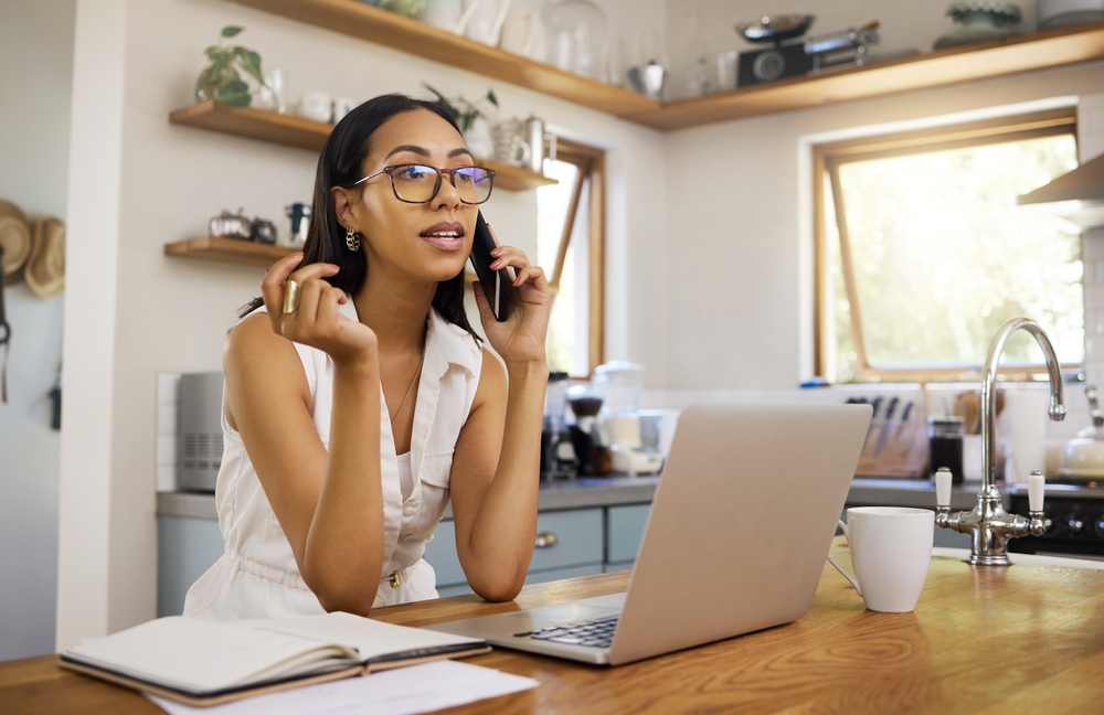 Young woman talking on the phone while taking notes and using laptop