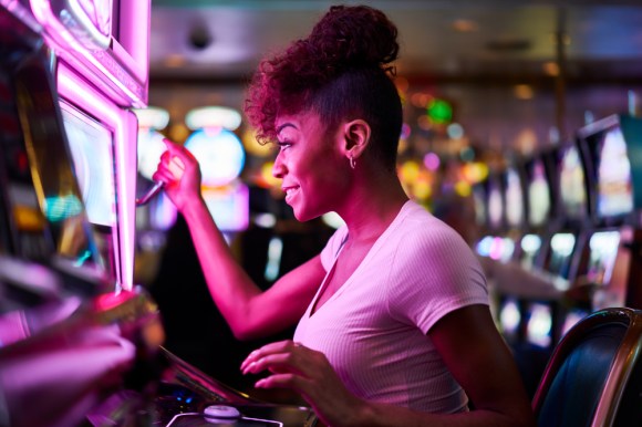 Young Black woman playing slot machine.