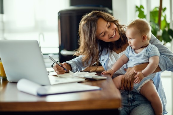 Woman sitting at a table preparing her taxes with a baby on her lap.
