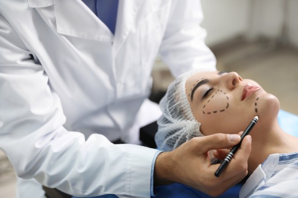 Patient laying down while cosmetic surgeon marks their face for treatment.
