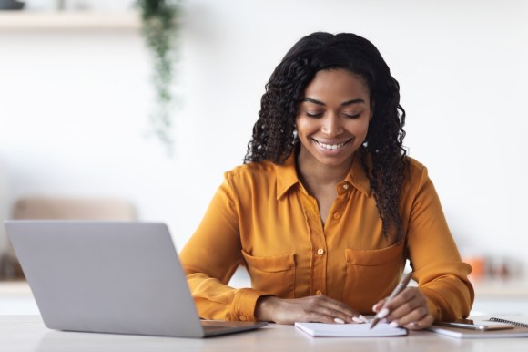 Young Black woman smiling and writing.
