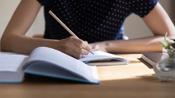 Close-up of a textbook and woman writing in a notebook.