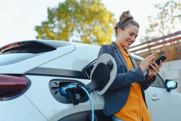 Young woman using her phone while charging her electric vehicle.