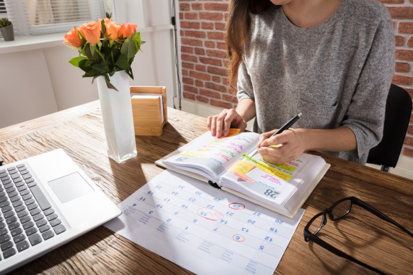Woman marking her calendar and writing in personal planner.