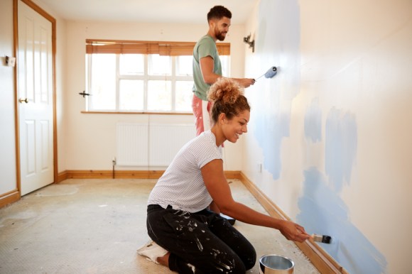 A couple painting a wall inside of their home together.