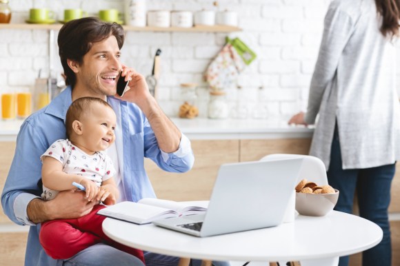 Caucasian father sitting with a baby on his lap while making a phone call.