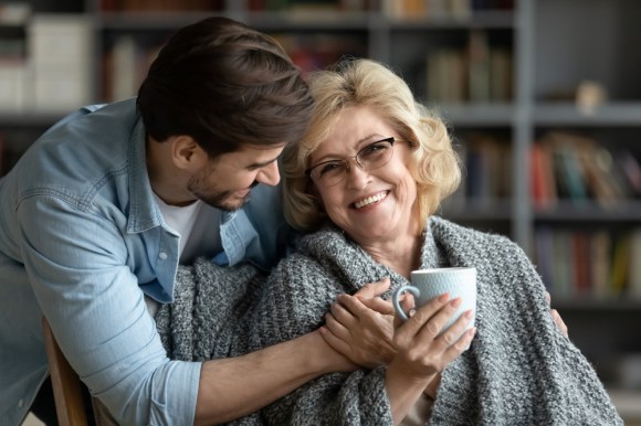 Man handing a cup of coffee to his elderly mother.
