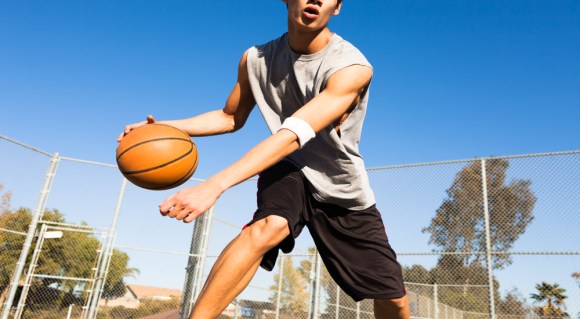 Male student-athlete playing basketball outside.