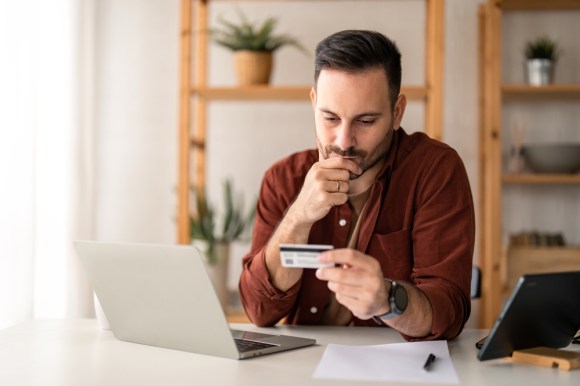 Man looking at a credit card with a contemplative look on his face.