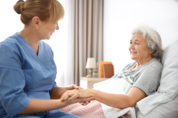 Care worker holding an elderly lady’s hand while she rests in bed.
