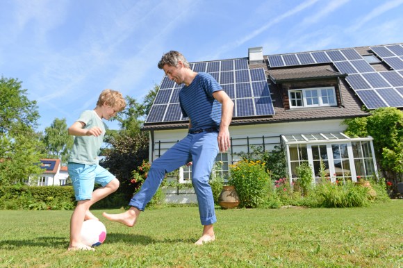 Father and son playing in front of a house with solar panels.
