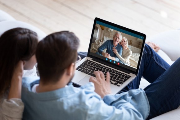 Couple communicating with elderly parents living abroad using a video call application on a laptop.