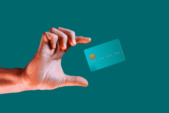 Close-up male hand reaching for a levitating mock credit card isolated on a green background.
