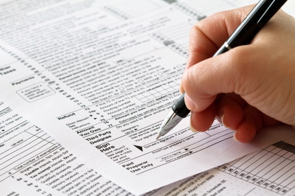 A close-up shot of a hand with a pen filling out a tax form.
