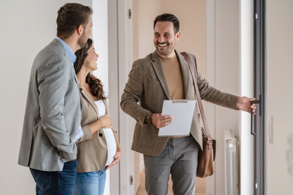 Real estate agent speaking to an expecting couple while they browse a home.