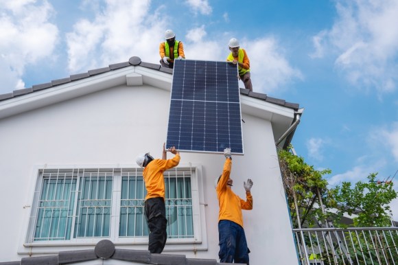 Group of men installing solar panels on the roof of a house.

