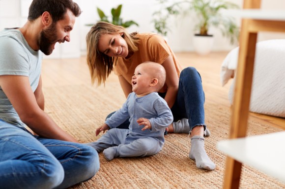 New parents playing with their baby on the floor.
