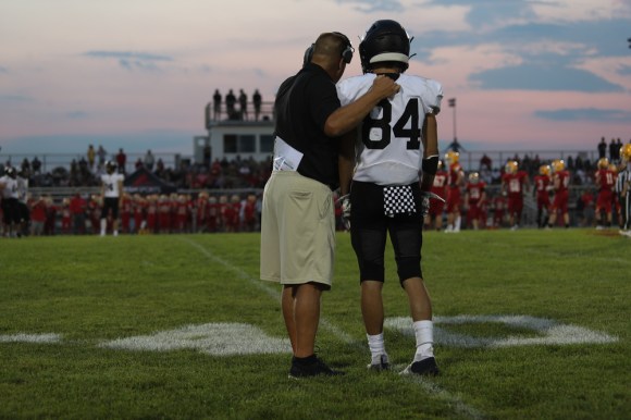  High-school football coach standing on the sidelines with player.