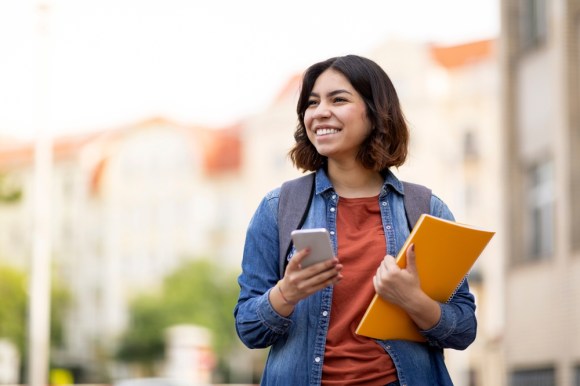 College student on her way to class holding book and phone.