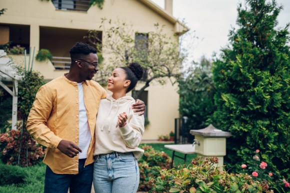 Young Black couple standing outside of their new home.