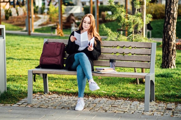 College student reading a document on a bench.
