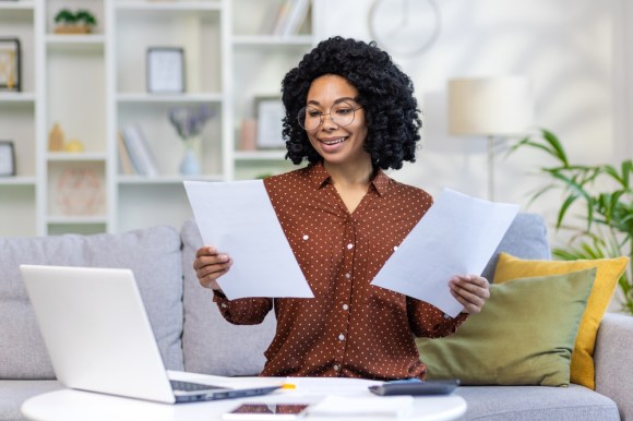 Black woman sitting on couch reviewing paperwork.