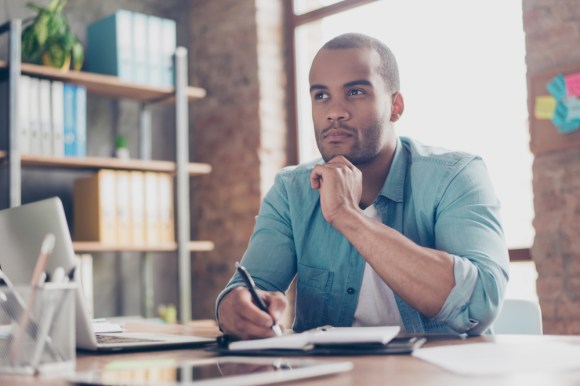 Young Black man considering a decision while sitting at his desk.