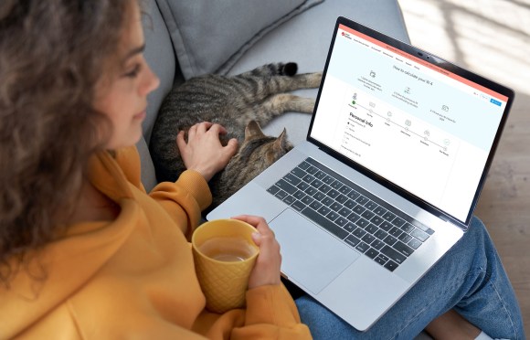 Young hispanic latin teen girl student relax sit on sofa with cat holding laptop looking at mock up white computer screen online learning on pc, elearning, watching movie. Over shoulder closeup view; 