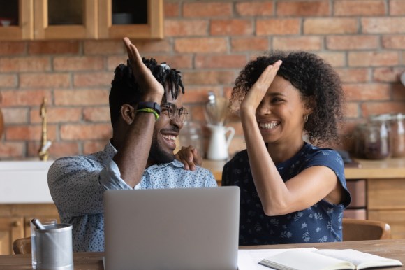 Young Black couple high-fiving at dinner table while working on taxes.