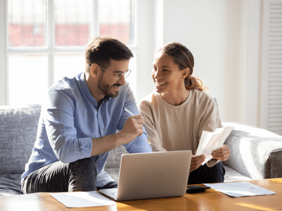 Man and woman looking at a toptop with papers and a book on the table.