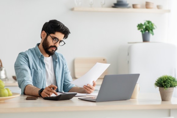 Young man using a calculator and reviewing a document