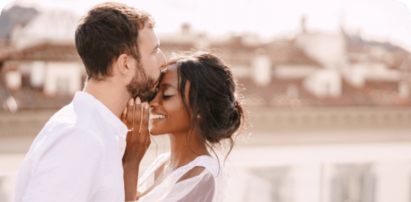 Photo of a man and woman dressed in white smiling and embracing each other