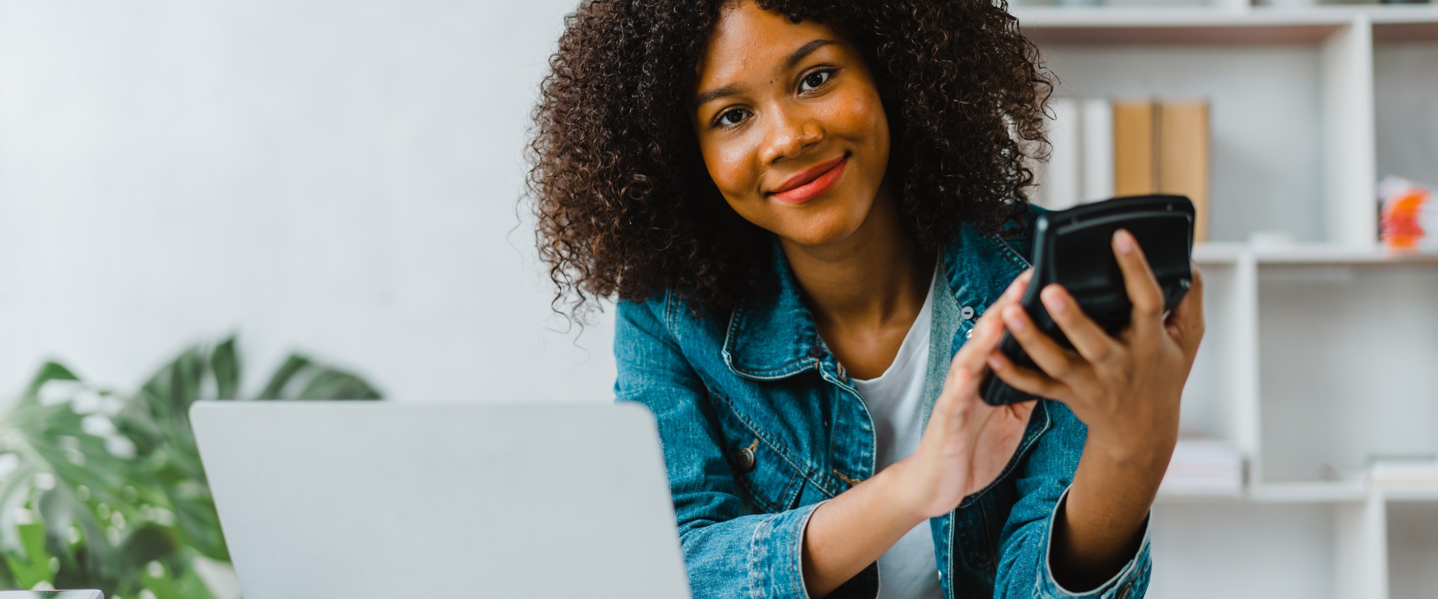 Smiling young Black woman sitting in home office using a calculator.