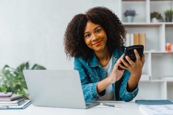 Smiling young Black woman sitting in home office using a calculator.