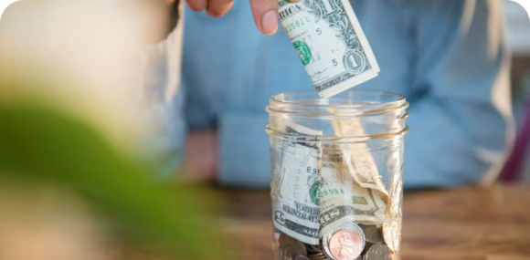 Photo of a person putting dollars and coins into a glass jar