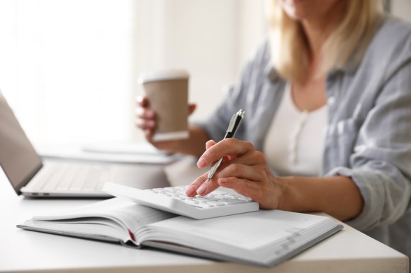 Close-up of blonde woman using a calculator and drinking coffee.